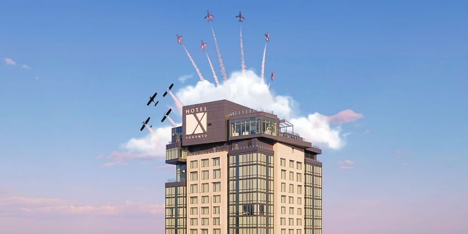 Modern high-rise hotel building with large logo sign under blue sky with flying airshow jet planes at Hotel X Toronto