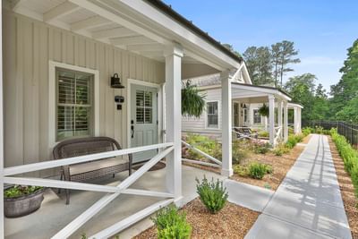 Modern cottage with porches, lush greenery, and paved walkway under clear blue sky by Cottages at Laurel Brooke