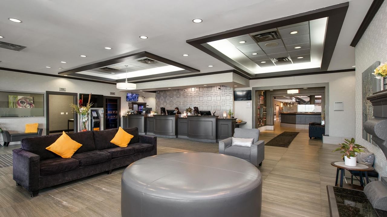 Modern hotel lobby with dark sofas, orange accent pillows, and reception desk at Coast Calgary University Area Hotel by APA
