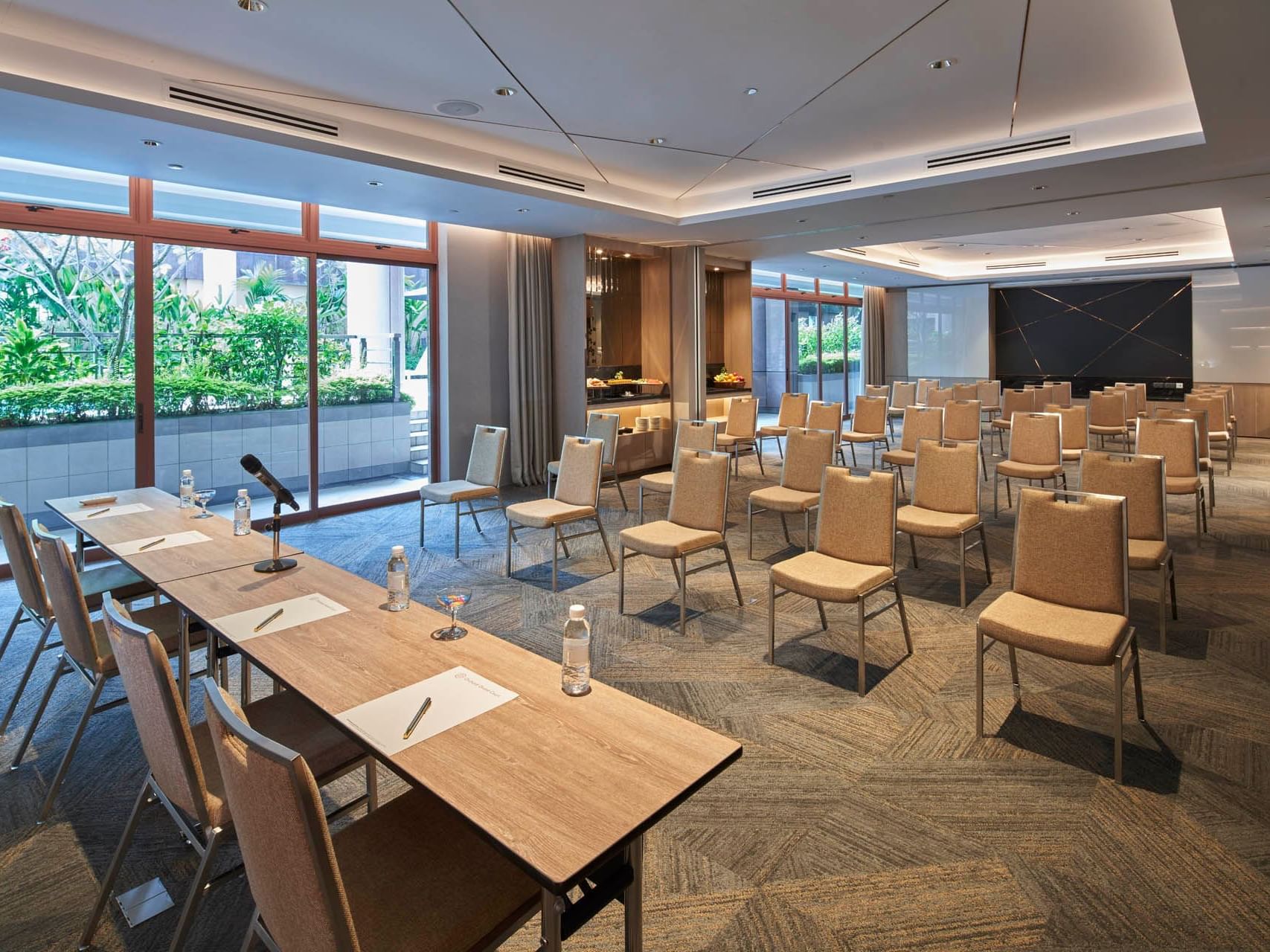 Contemporary conference room with rows of chairs, a wooden table, a microphone, and large windows at Orchard Grand Court