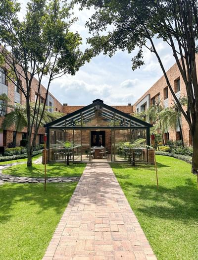 Glass-enclosed dining in La Tiendita Steak House in a serene courtyard with lush greenery at Habitel Prime Hotel