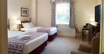 Two queen beds, desk and chair with TV on dresser.