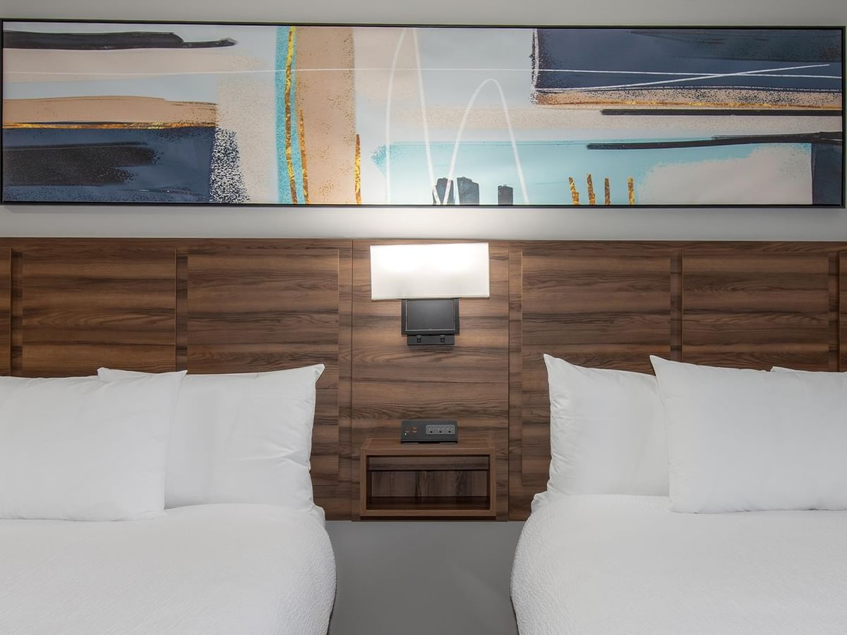 Two beds with white linens and a modern art piece.