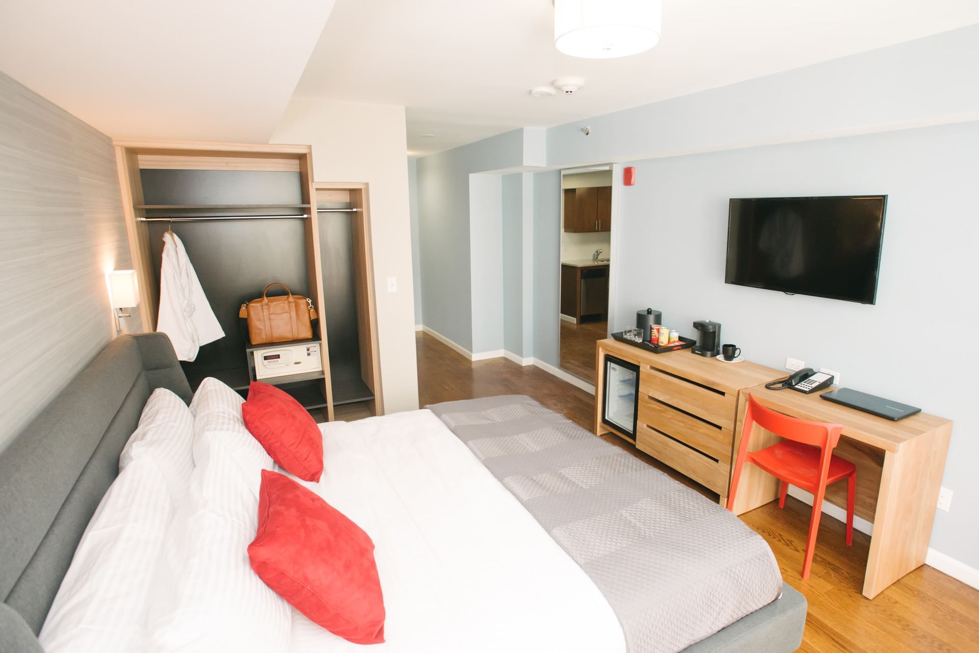 A hotel room with a king-sized bed, desk, TV, mini-fridge, and kitchenette.