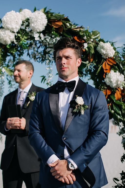 A groom waits under the arch for his bride at our Diamond Beach wedding venue