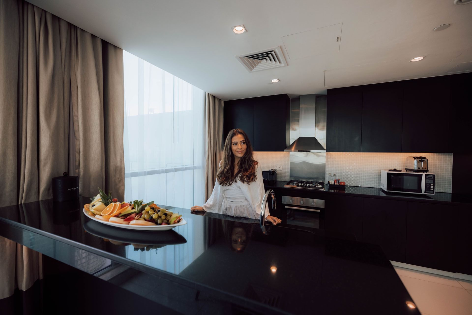 Lady by the countertop with a plate of fruit in kitchen at DAMAC Maison Distinction