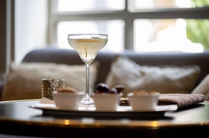 Glass of cocktail on table with snacks and couch in background at Barsey by Warwick 