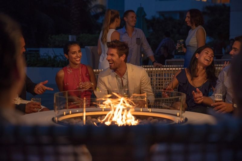Lively gathering around a circular fire pit, with guests enjoying drinks and conversation at The Diplomat Resort