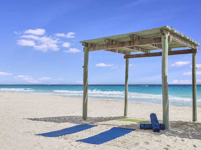 Yoga mats on sandy shore by shady wooden hut overlooking the sea at Live Aqua Cancún