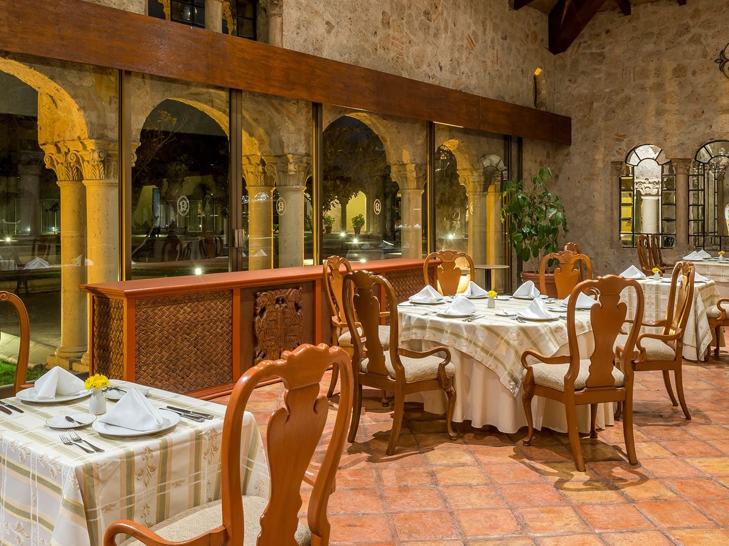 Elegant restaurant with stone walls, arched windows, terracotta floors, and white-clothed tables at Quinta Real Aguascalientes