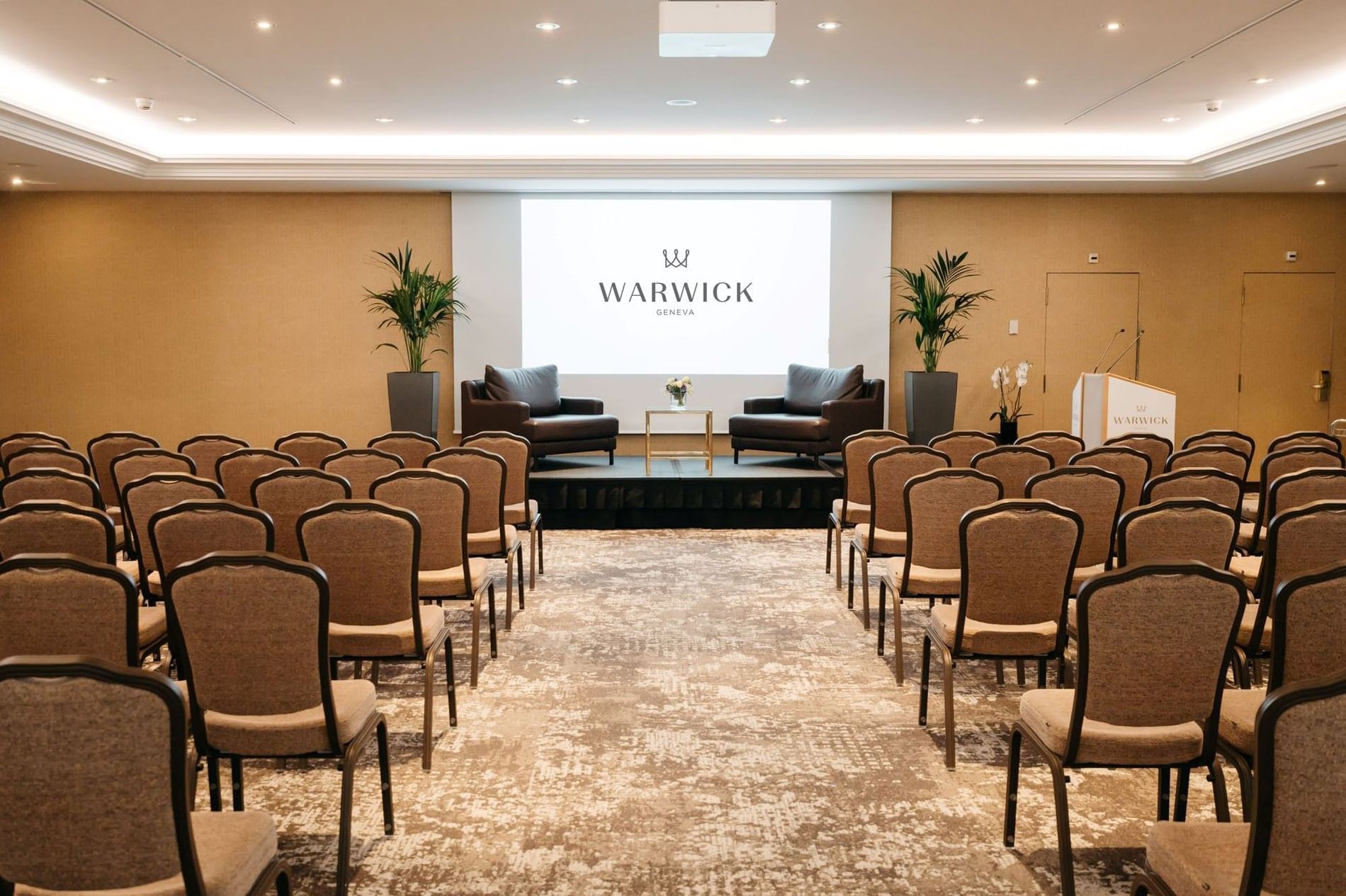 Leather armchairs by a gold table on a stage in front of guest chairs in Mont-Blanc + Jura at Warwick Geneva