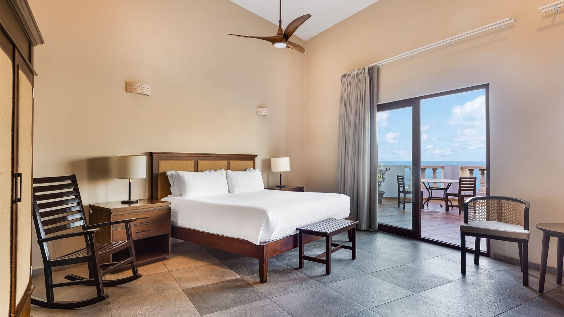 Spacious room featuring a bed, rocking chair, and a balcony with an ocean view at Curamoria Collection