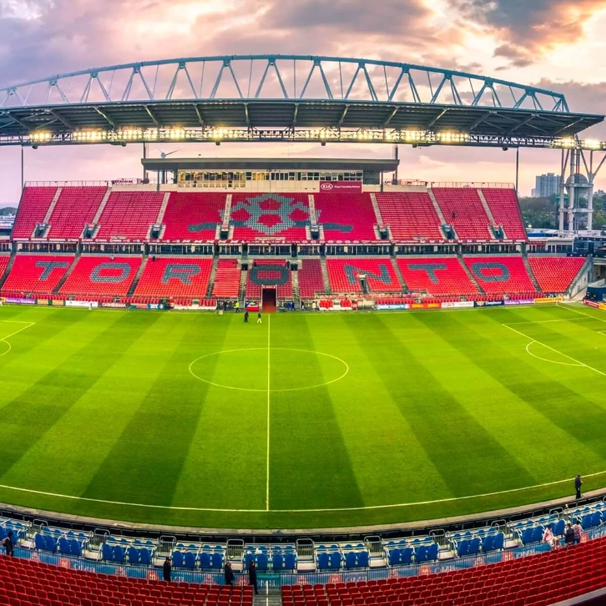 BMO Field with green soccer pitch by red Toronto seating under a glowing sunset sky near Hotel X Toronto