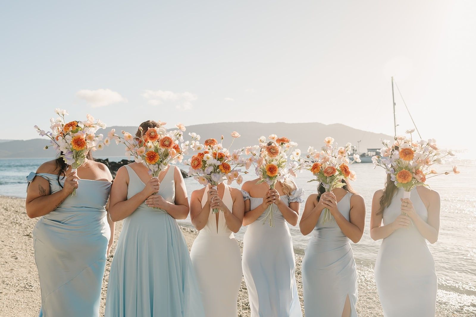 The beautiful bride and her bridesmaids hold their bright floral bouquets in front of their faces at Daydream Island