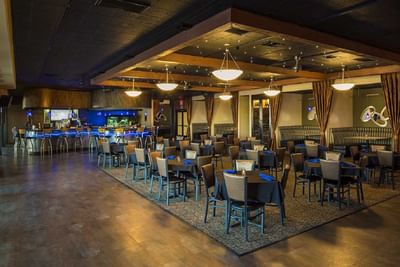 Spacious restaurant and bar area with pendant lighting, booth seating, and blue napkins on tables at London Bridge Resort
