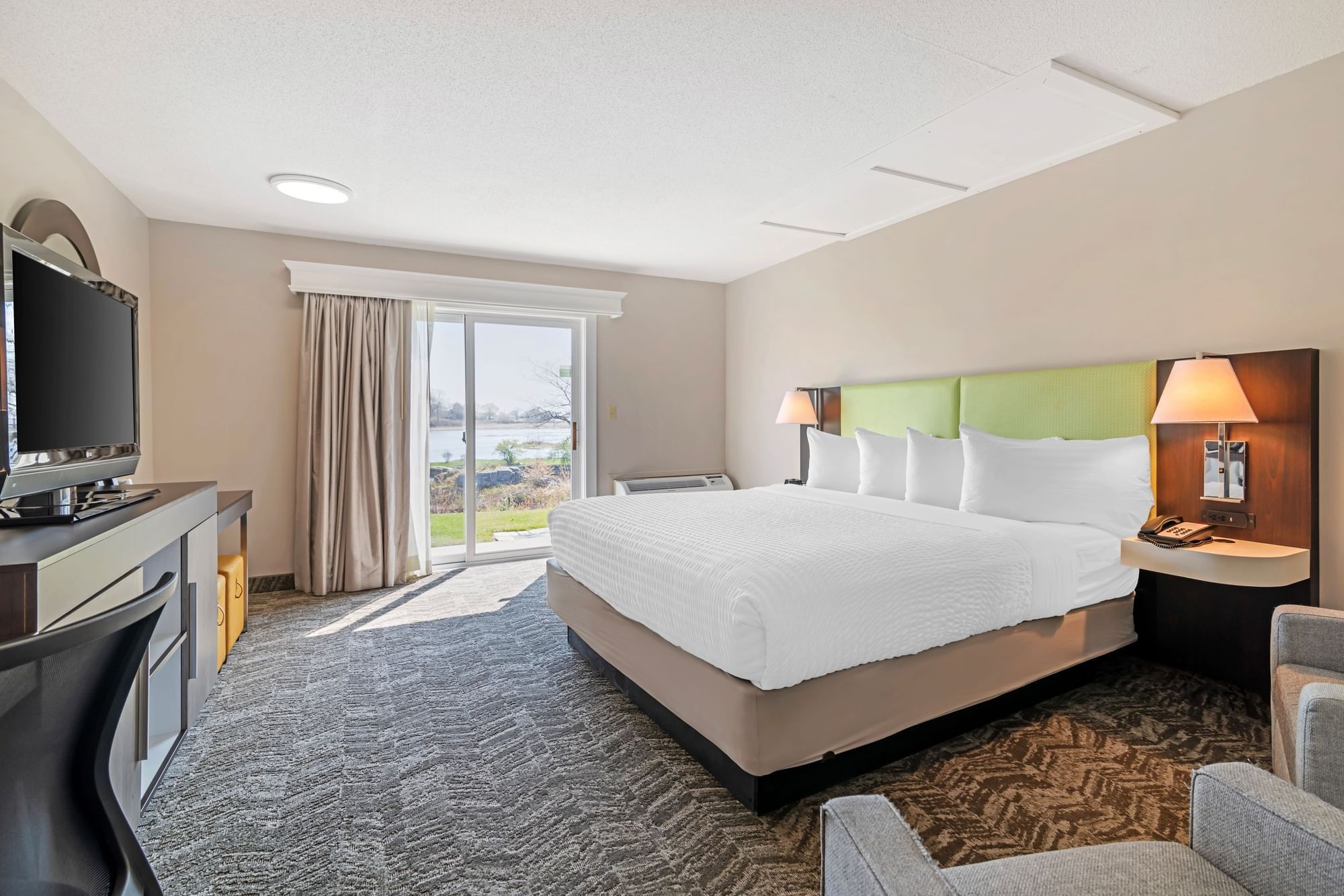 A hotel room with a large bed, TV, desk, and sliding glass door