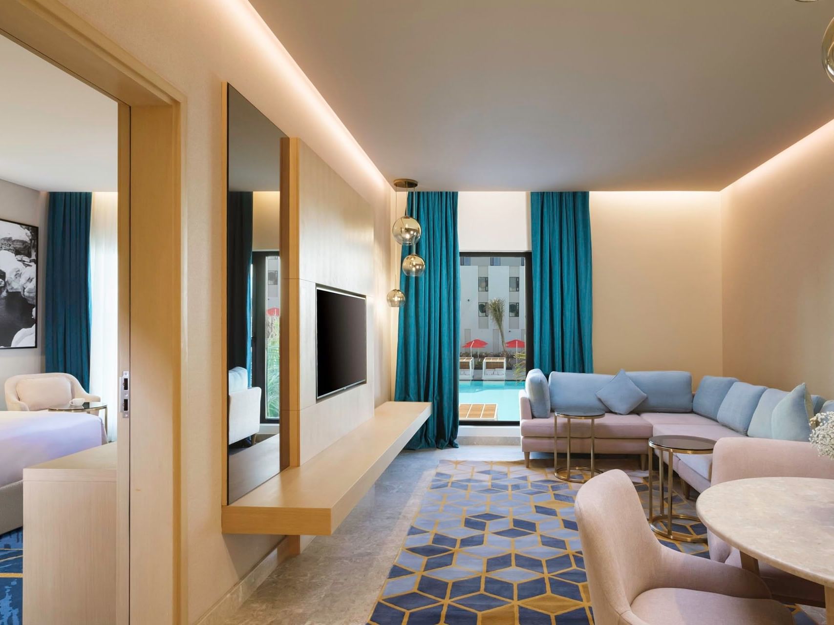 A luxurious hotel room with a bed, living area, pool view, and modern decor.