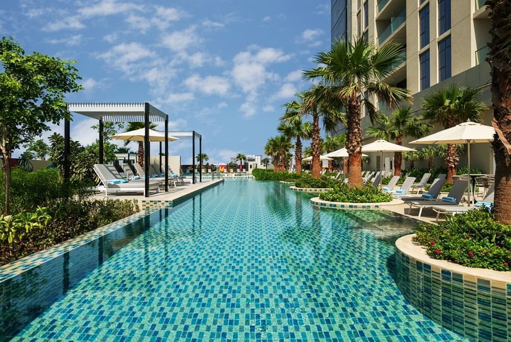 Outdoor pool with sun loungers and patio umbrellas at DAMAC Maison Aykon City
