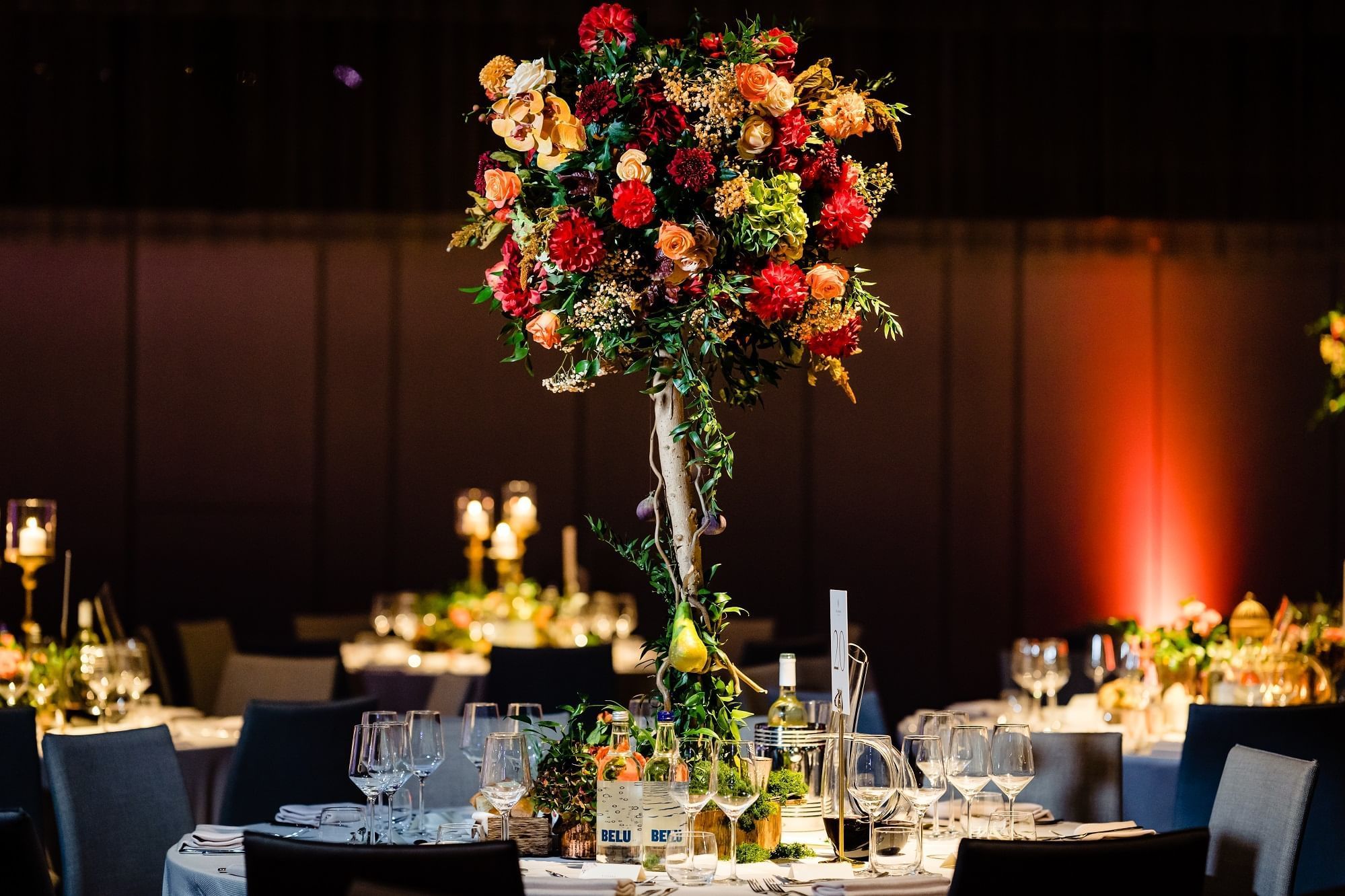 Tables with a floral centerpiece, lit candles, and glasses in a wedding ceremony at The Londoner Hotel