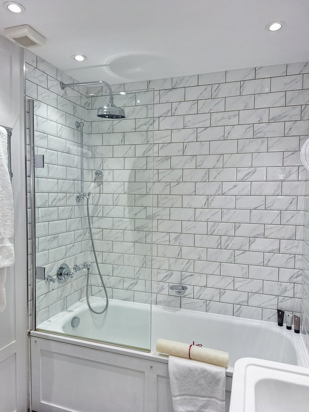 White bathroom with bathtub, shower, and towel at The Capital Hotel, Apartments & Townhouse - London.