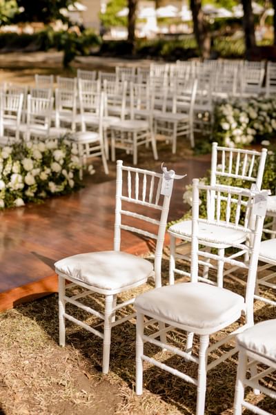 Close-up of white chairs set up with floral decor in an outdoor event at El Mangroove Hotel
