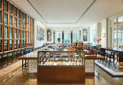 Dining area with display of colorful pastries, wooden decor, and airy atmosphere in The Pastry Boutique at Park Hyatt Saigon