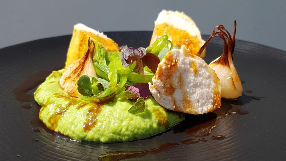 Roasted chicken by a green pea puree and charred onions on a black plate at Warwick Paris Champs Elysées