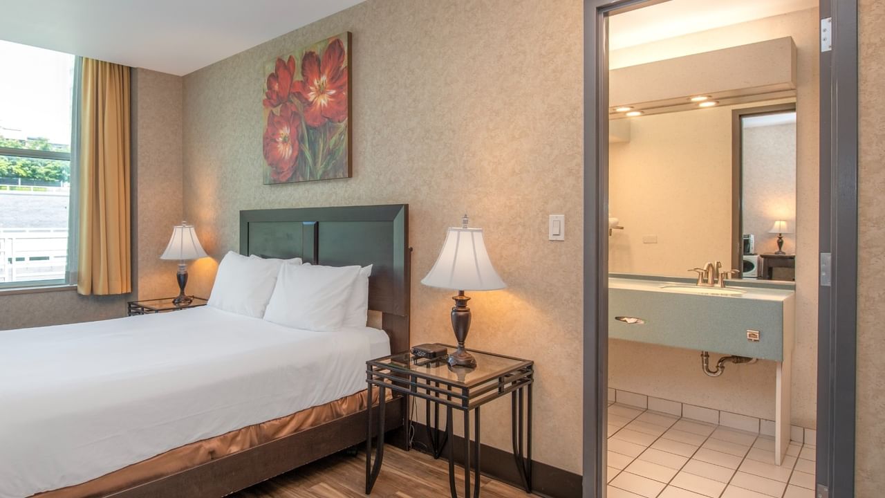 Coast Queen room with a bed, two nightstands with lamps, and a bathroom with a sink at Coast Lonsdale Quay Hotel