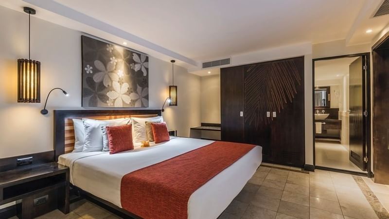 King bed by dark wood closets under floral art near a bright ensuite bath in Warwick Suites at Warwick Fiji Resort and Spa