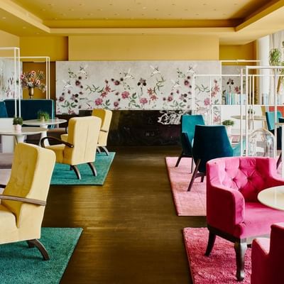Elegantes Hotellobby mit bunten Stühlen, Tischen und floralen Wanddekorationen.