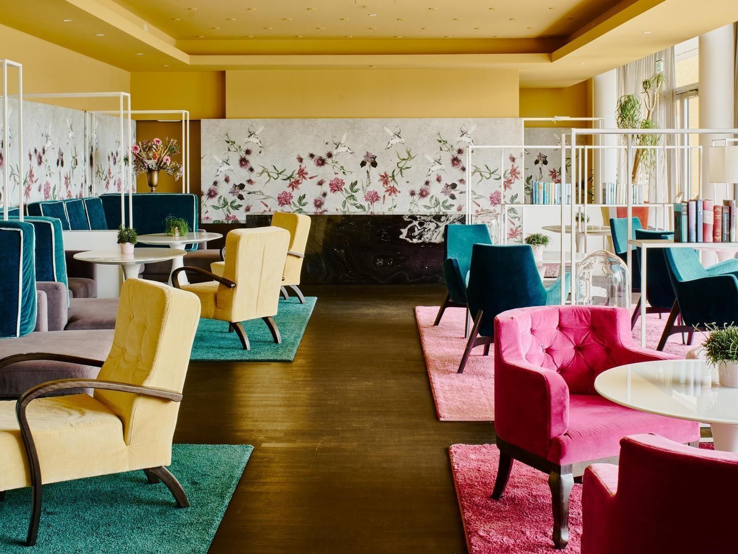 Brightly lit lounge area with colorful chairs, floral wall decor, and small plants on tables.