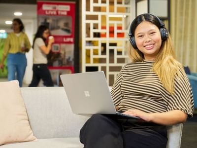 Smiling resident using laptop and headphones on couch at Student Living on Villiers.