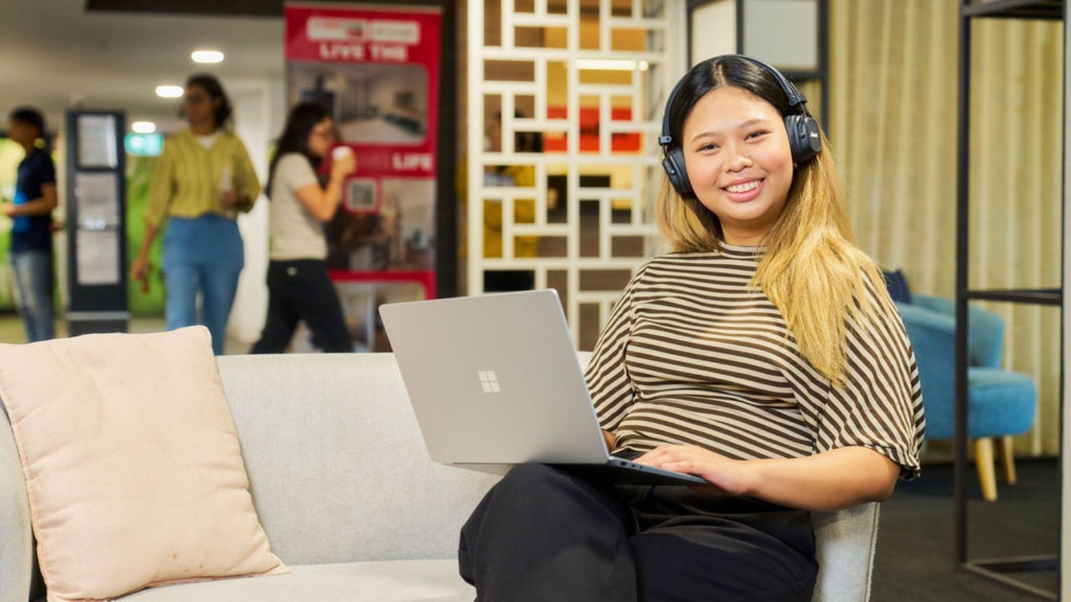 Smiling resident using laptop and headphones on couch at Student Living on Villiers.
