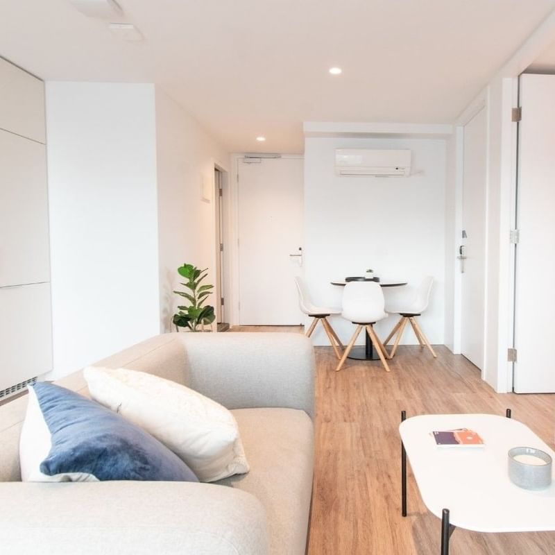 White living room with couch, coffee table, TV, and dining set in the background.