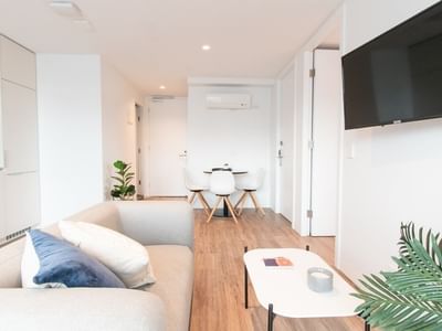 White living room with couch, coffee table, TV, and dining set in the background.
