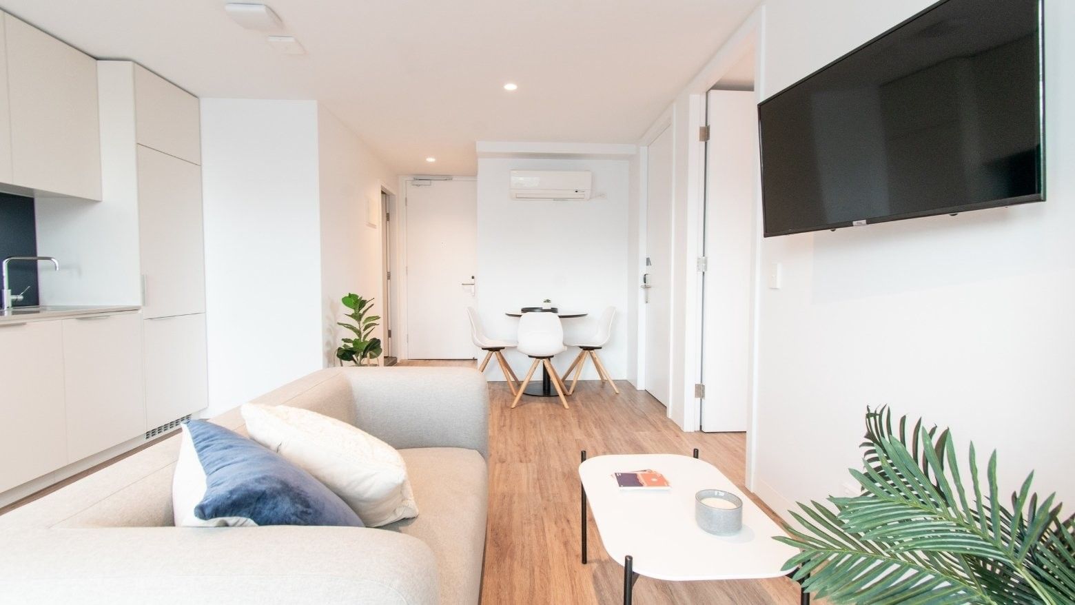 White living room with couch, coffee table, TV, and dining set in the background.