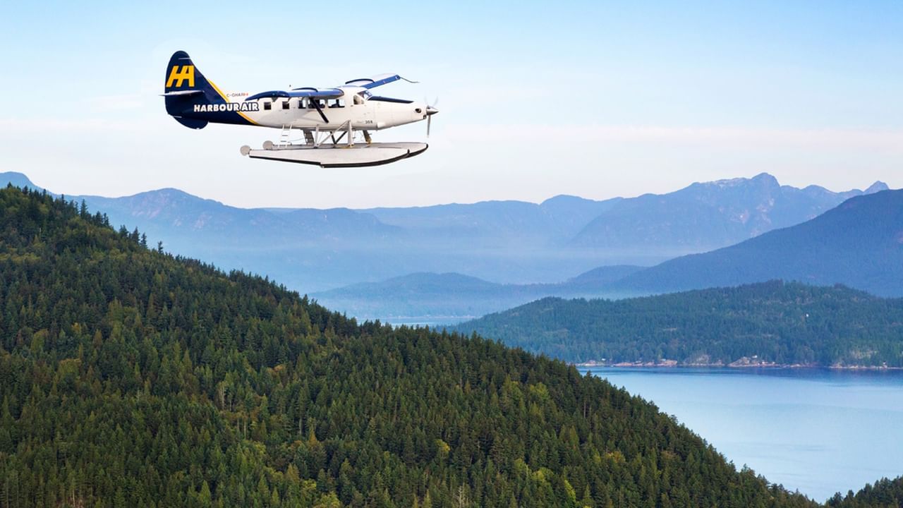 Harbour Air seaplane flying above a forested hillside and serene lake.
