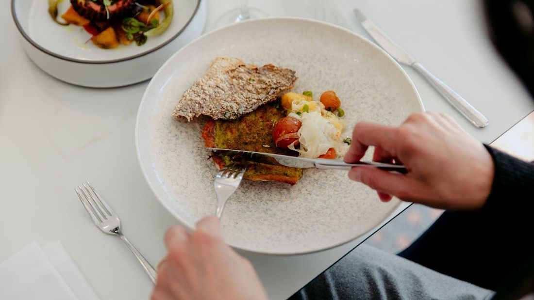 A person holds a knife and fork over a plate of food on a table with other dishes.