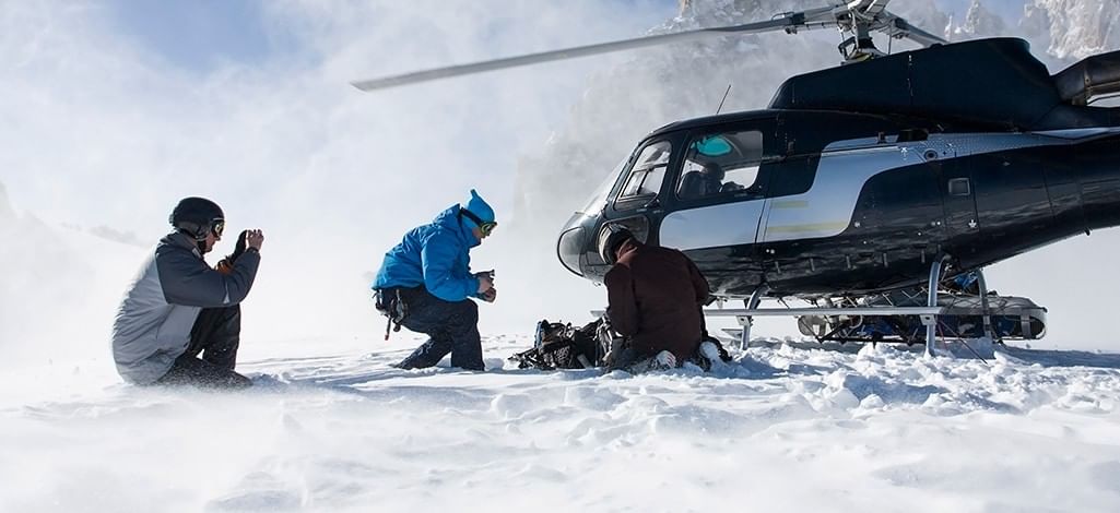 three snowboarders stepping out of a helicopter in the snow