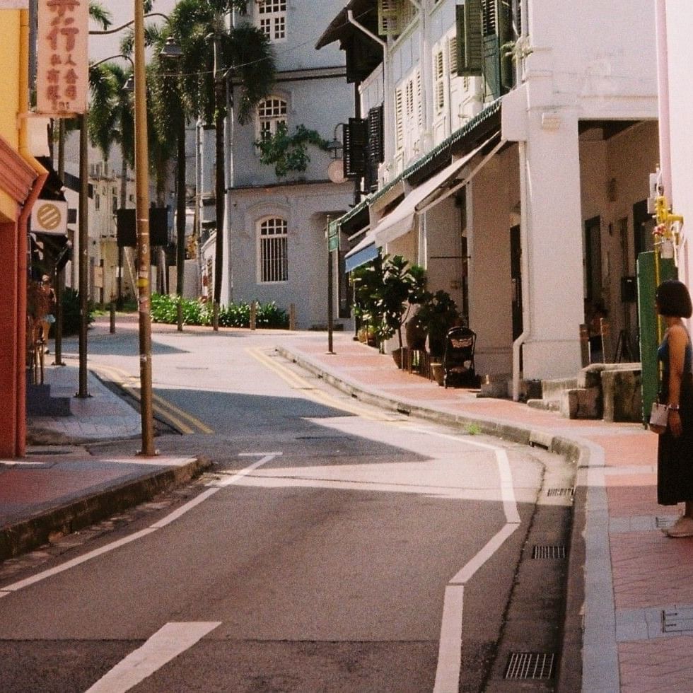 Woman standing on a sidewalk along a narrow urban street lined with historic shophouses near Grand Park City Hall