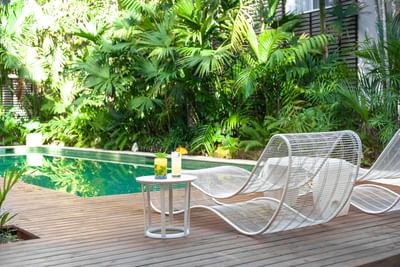 Sunny poolside with two modern lounge chairs and lush tropical greenery at Le Cameleon Boutique Hotel