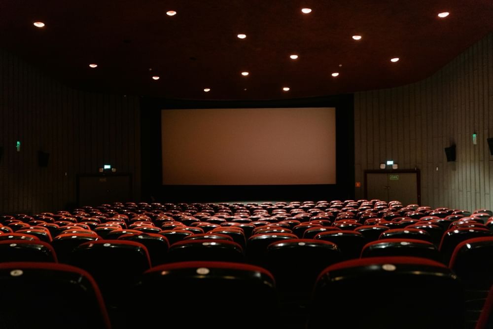 An empty movie theatre with rows of red chair facing a dark screen.