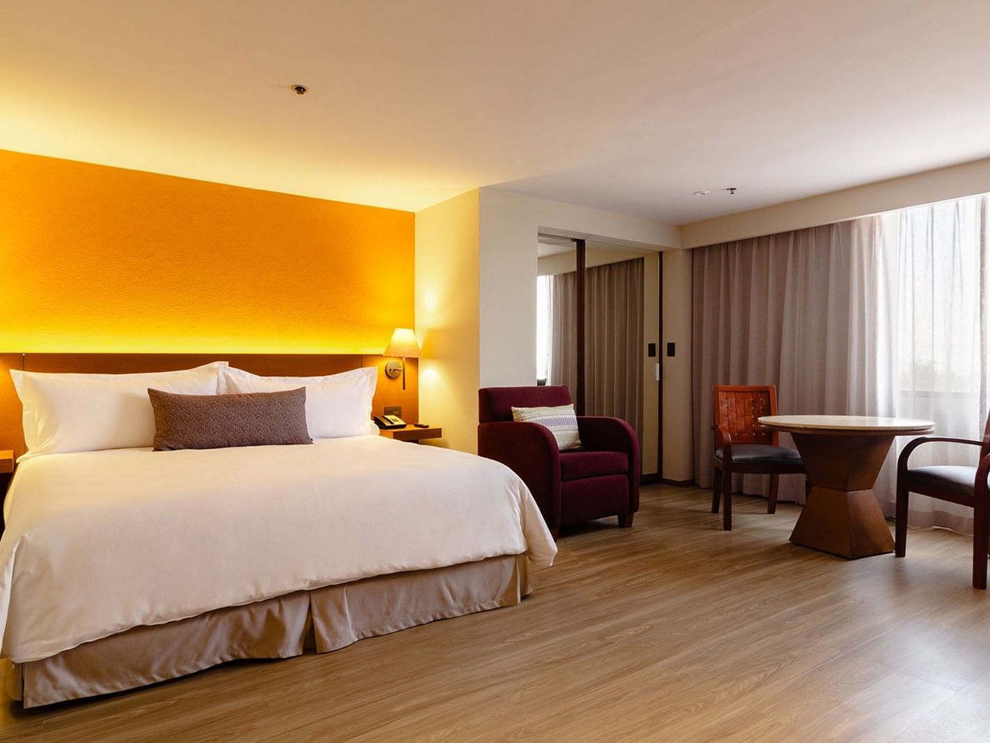 King bed with purple armchair, and a small dining table by the window in King Junior Suite at Camino Real Aeropuerto Mexico