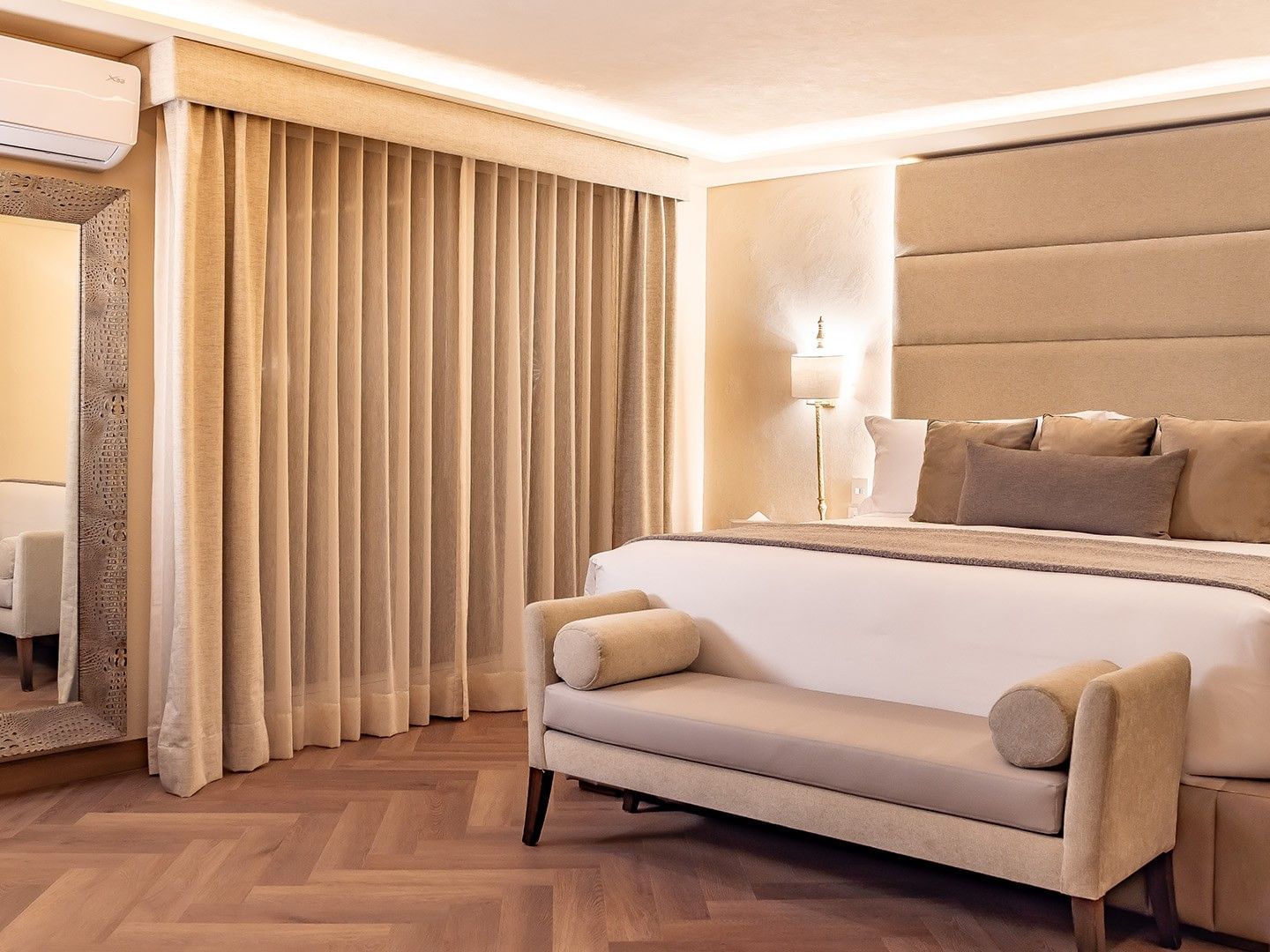 Habitación de hotel elegante con cama grande, sofá, espejo, cortinas y aire acondicionado.