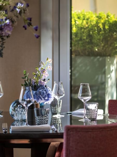 Glassware and blue flowers on a dark table by pink chairs in Terrace Le W at Warwick Paris Champs Elysées