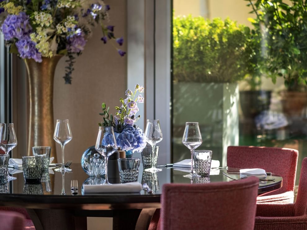 Glassware and blue flowers on a dark table by pink chairs in Terrace Le W at Warwick Paris Champs Elysées