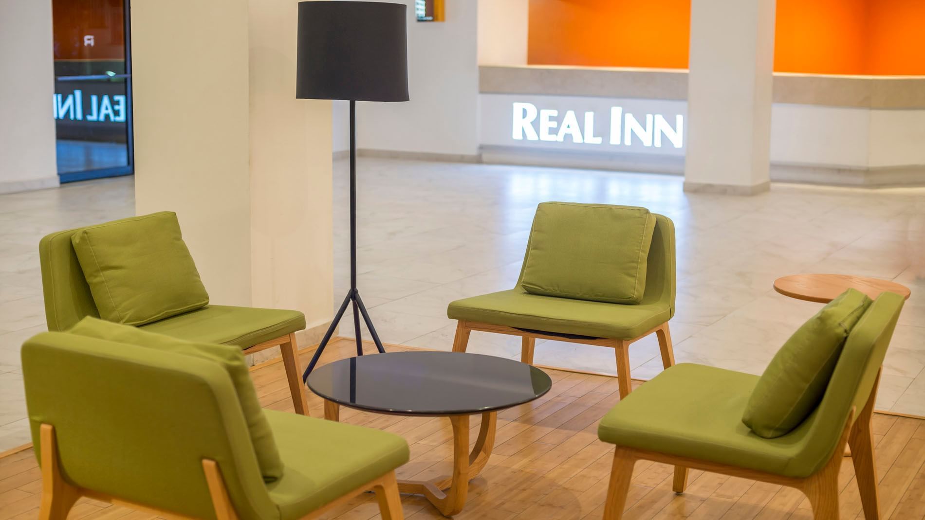 Green chairs by a black coffee table under a floor lamp in the lobby near the reception desk at Real Inn Mexicali
