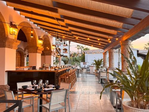 Patio del restaurante La Terraza del Santo al atardecer con bar y mesas preparadas para cenar en Hacienda del Mar Los Cabos.