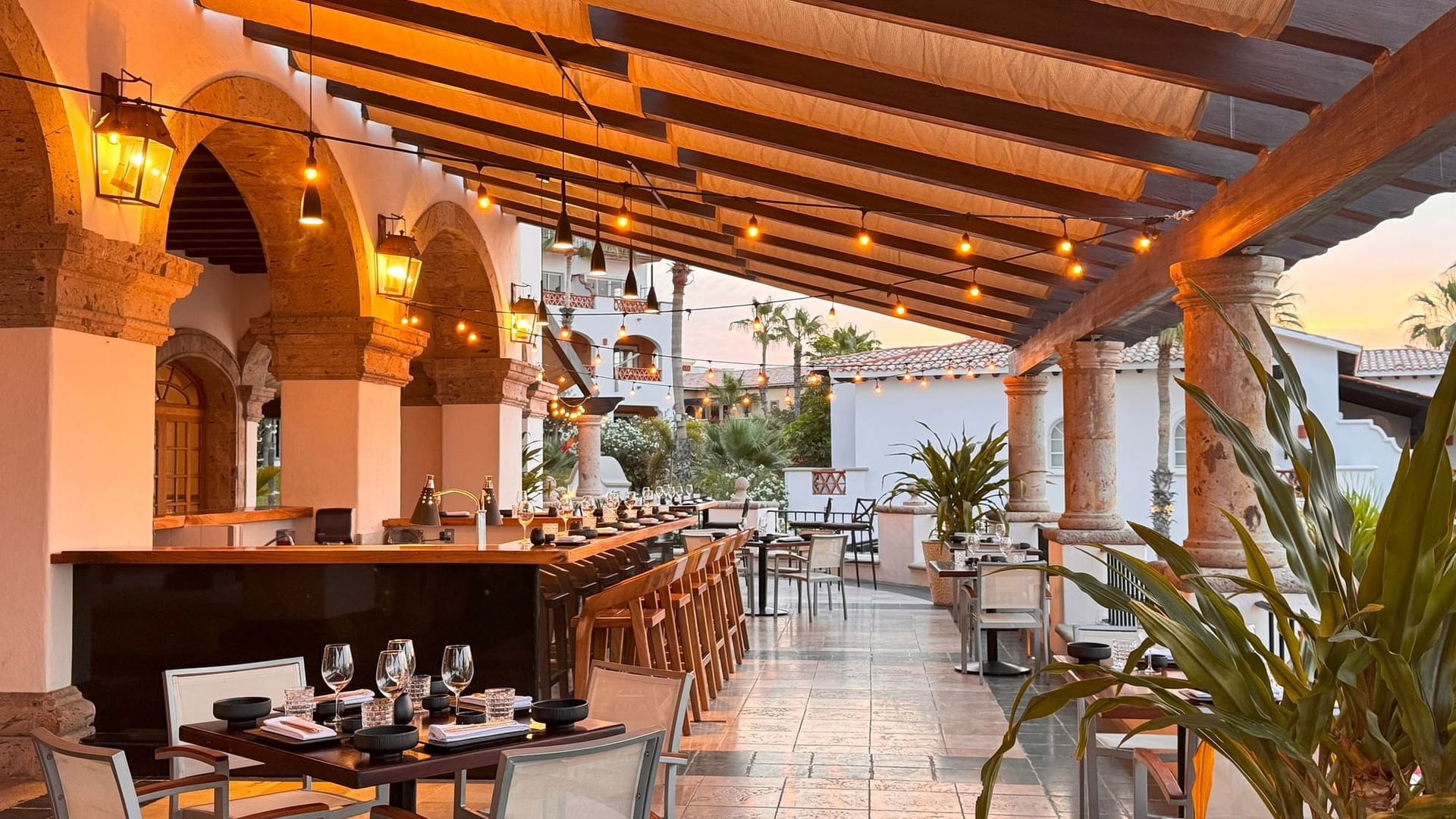 Patio del restaurante La Terraza del Santo al atardecer con bar y mesas preparadas para cenar en Hacienda del Mar Los Cabos.