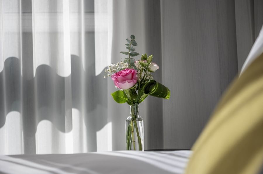 Vase with pink rose and green leaves on table next to bed at Warwick Le Crystal Montreal
